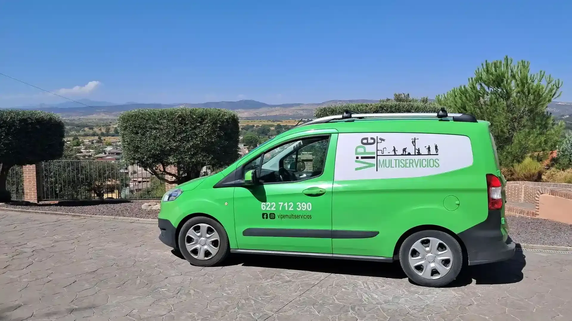 Furgoneta verde de servicio estacionada en una carretera asfaltada con un conductor. Vista de un paisaje con cielo azul.