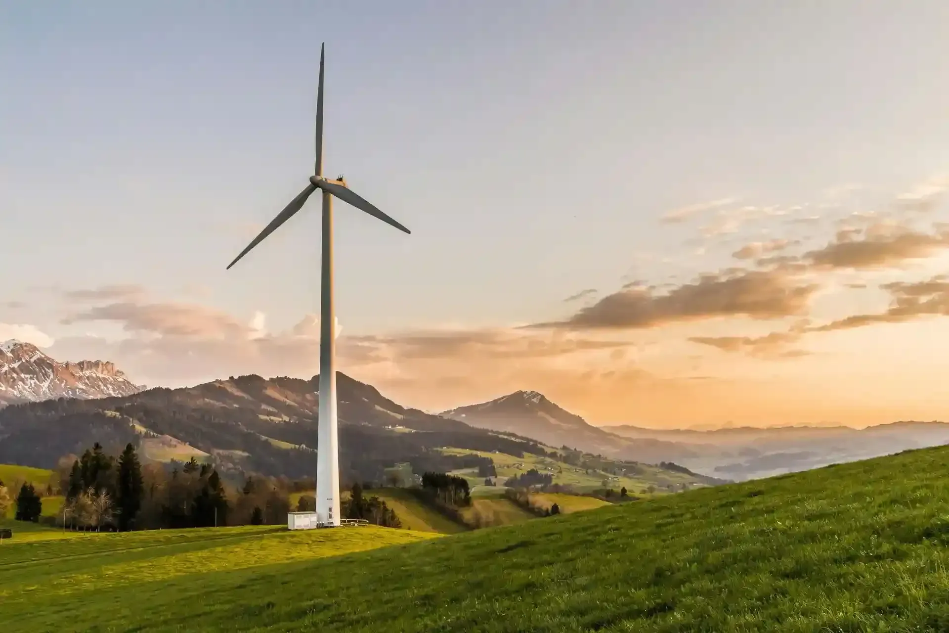 Aerogenerador en una ladera verde con montañas al fondo al atardecer.