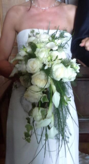 Une femme en robe blanche tient un bouquet de fleurs blanches.