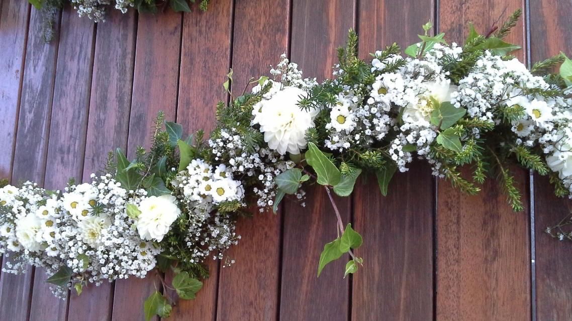 Une guirlande de fleurs blanches et de gypsophile est accrochée sur un mur en bois.