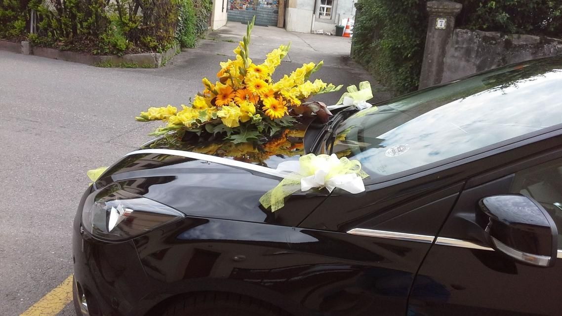 Une voiture noire avec des fleurs sur le capot est garée sur le bord de la route.