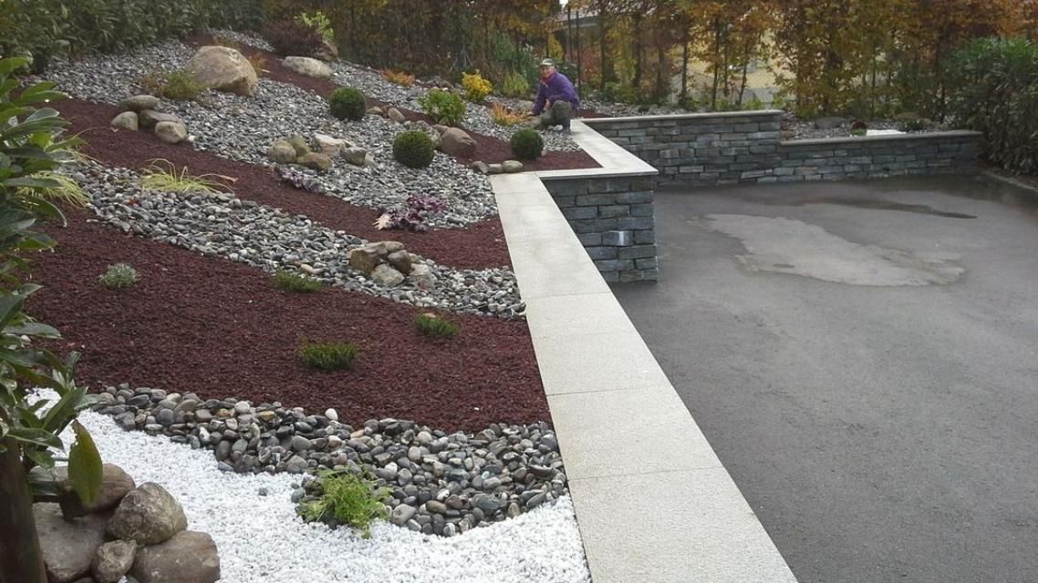 Un homme se tient debout dans un jardin entouré de rochers et de gravier.