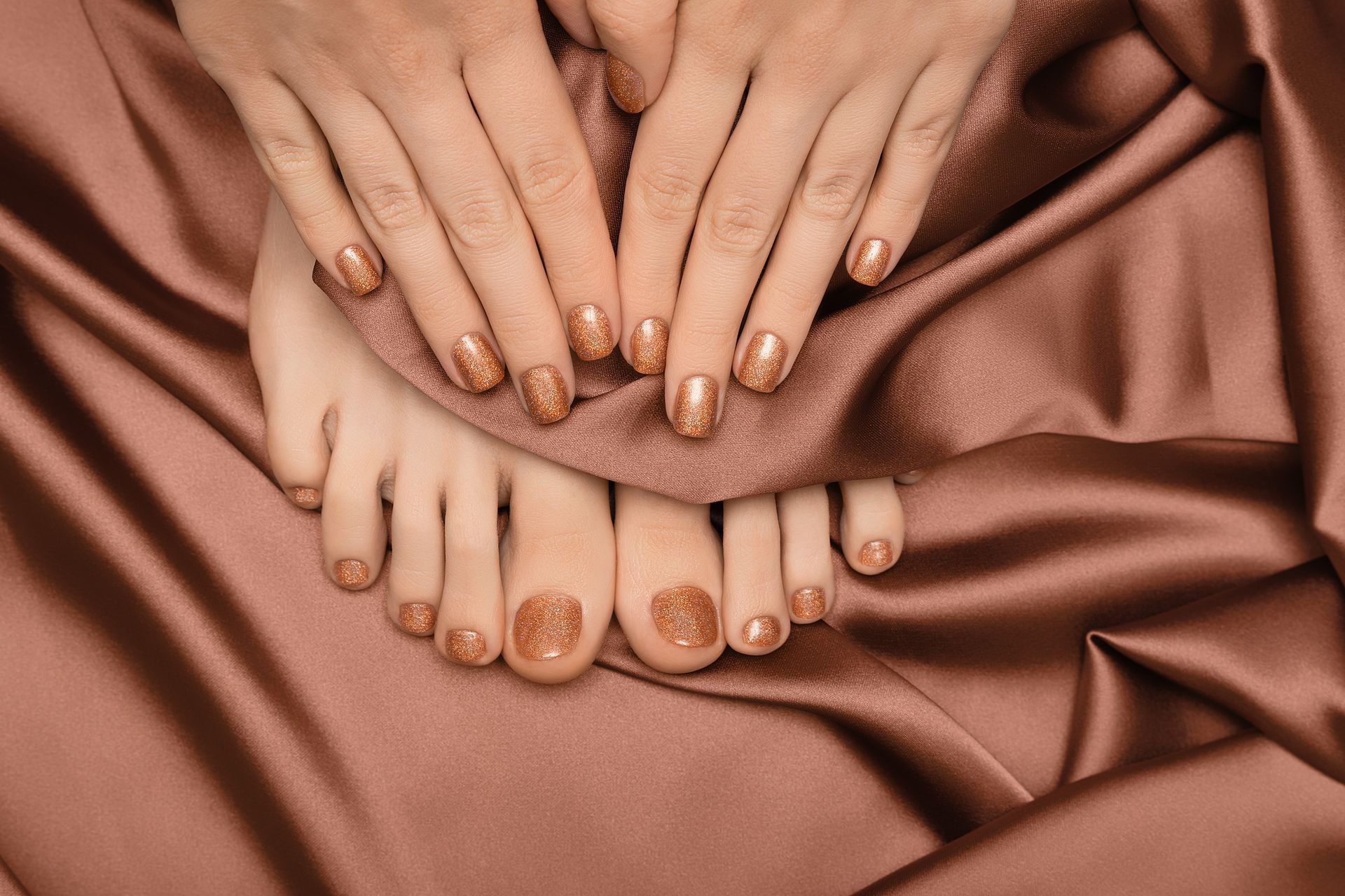 Hände und Füsse mit passendem goldenen Nagellack auf braunem Seidenstoff.