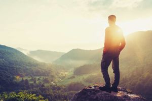Un hombre está parado en la cima de una montaña mirando la puesta de sol.