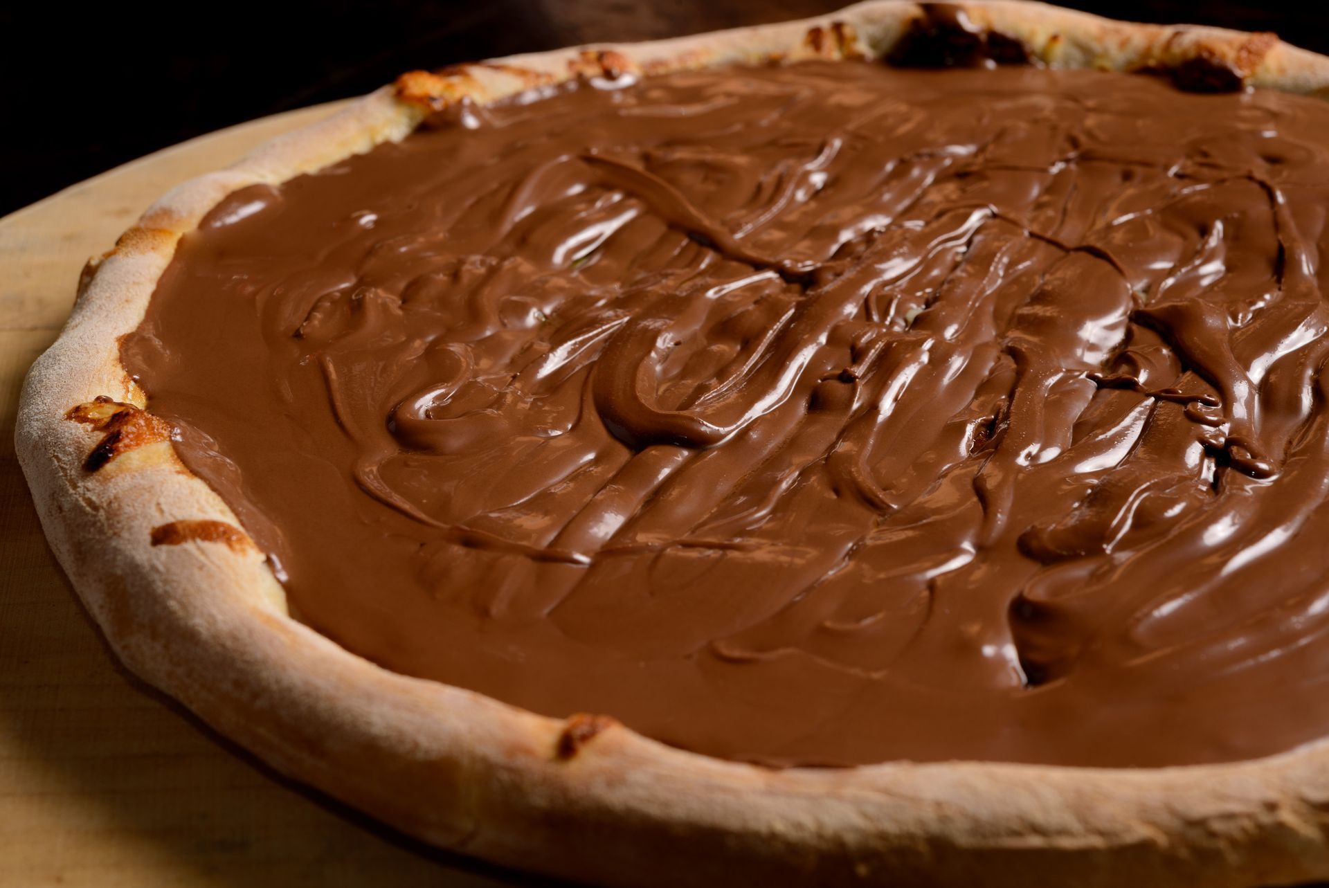 Una pizza con salsa de chocolate encima está sobre una mesa de madera.