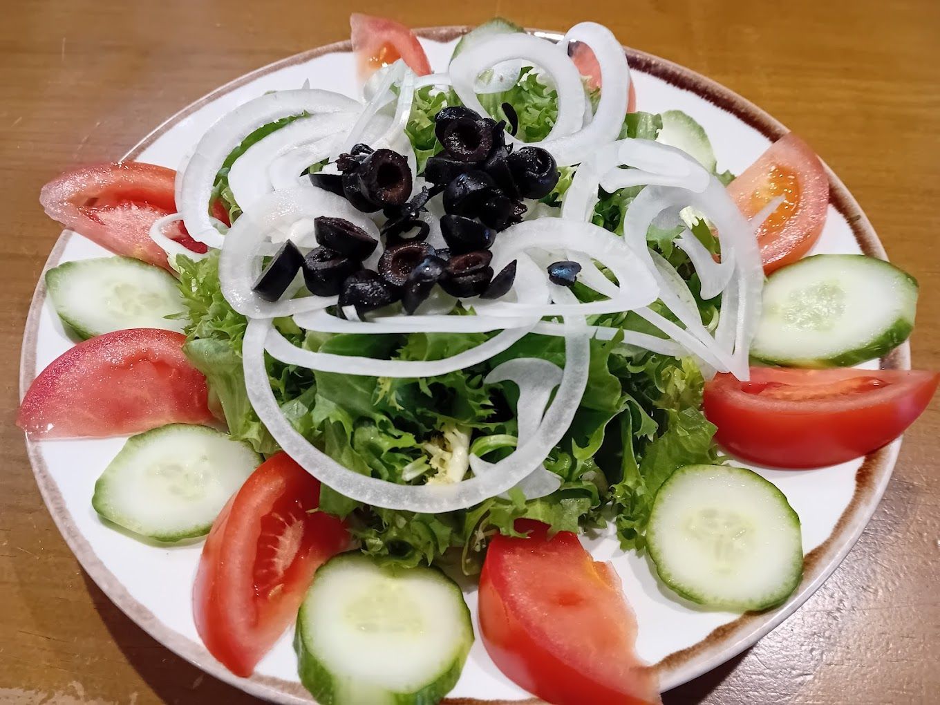 Una ensalada con tomates, pepinos, cebollas y aceitunas en un plato blanco