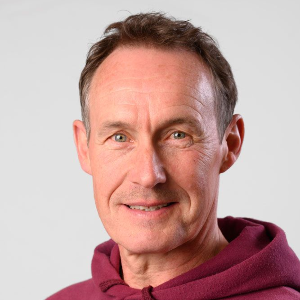 Ein Mann in einem roten Kapuzenpullover sitzt in der Tür eines roten Fahrzeugs und schaut in die Kamera.