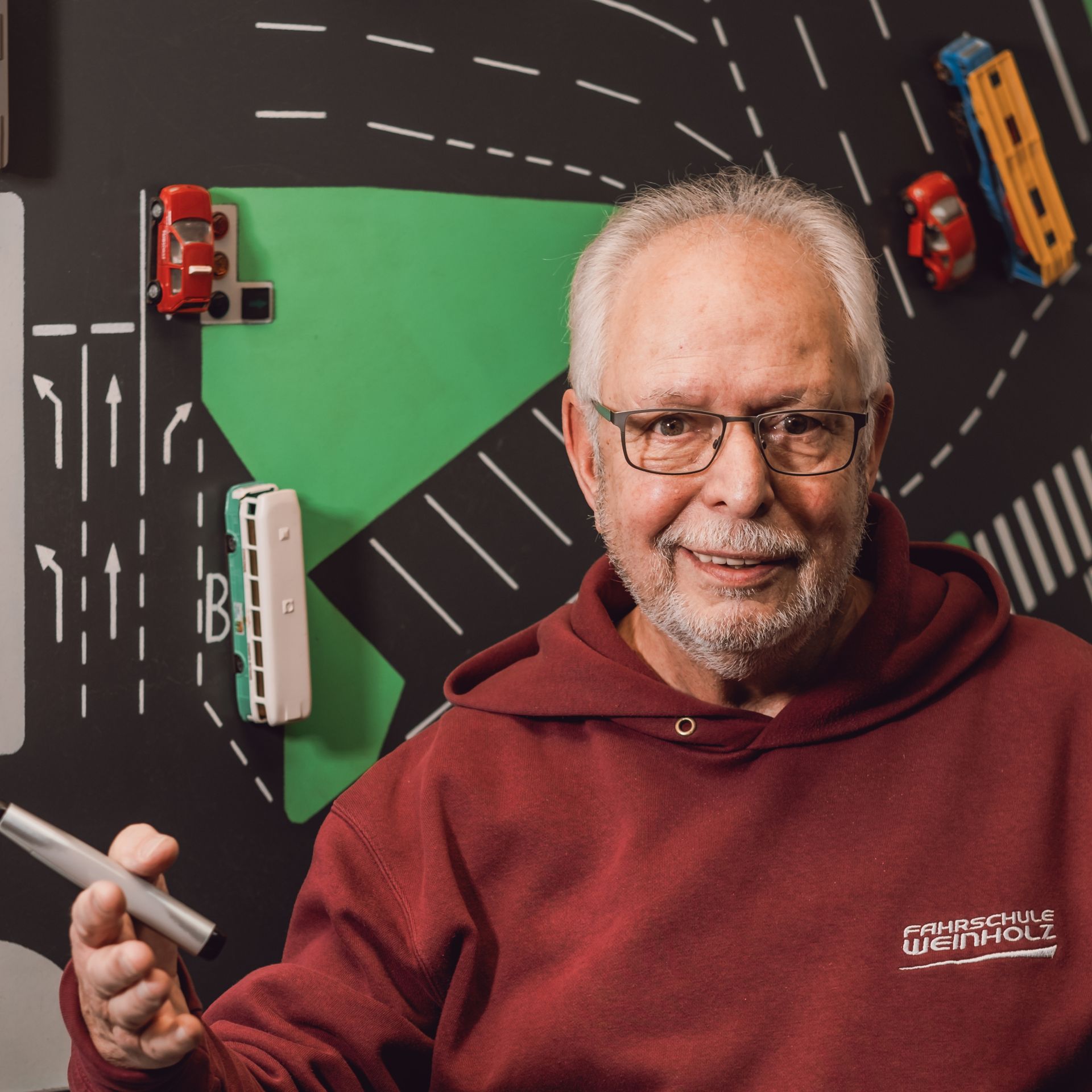 Mann hält einen weißen Stift vor einer Tischkarte mit Spielzeugautos und Straßenmarkierungen.