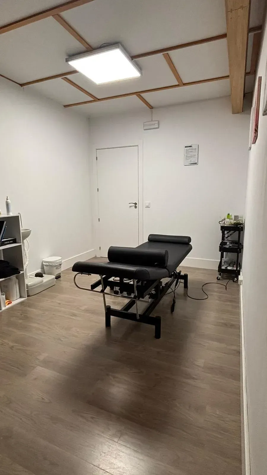 Sala de tratamiento quiropráctico con mesa negra, paredes blancas y suelo de madera.