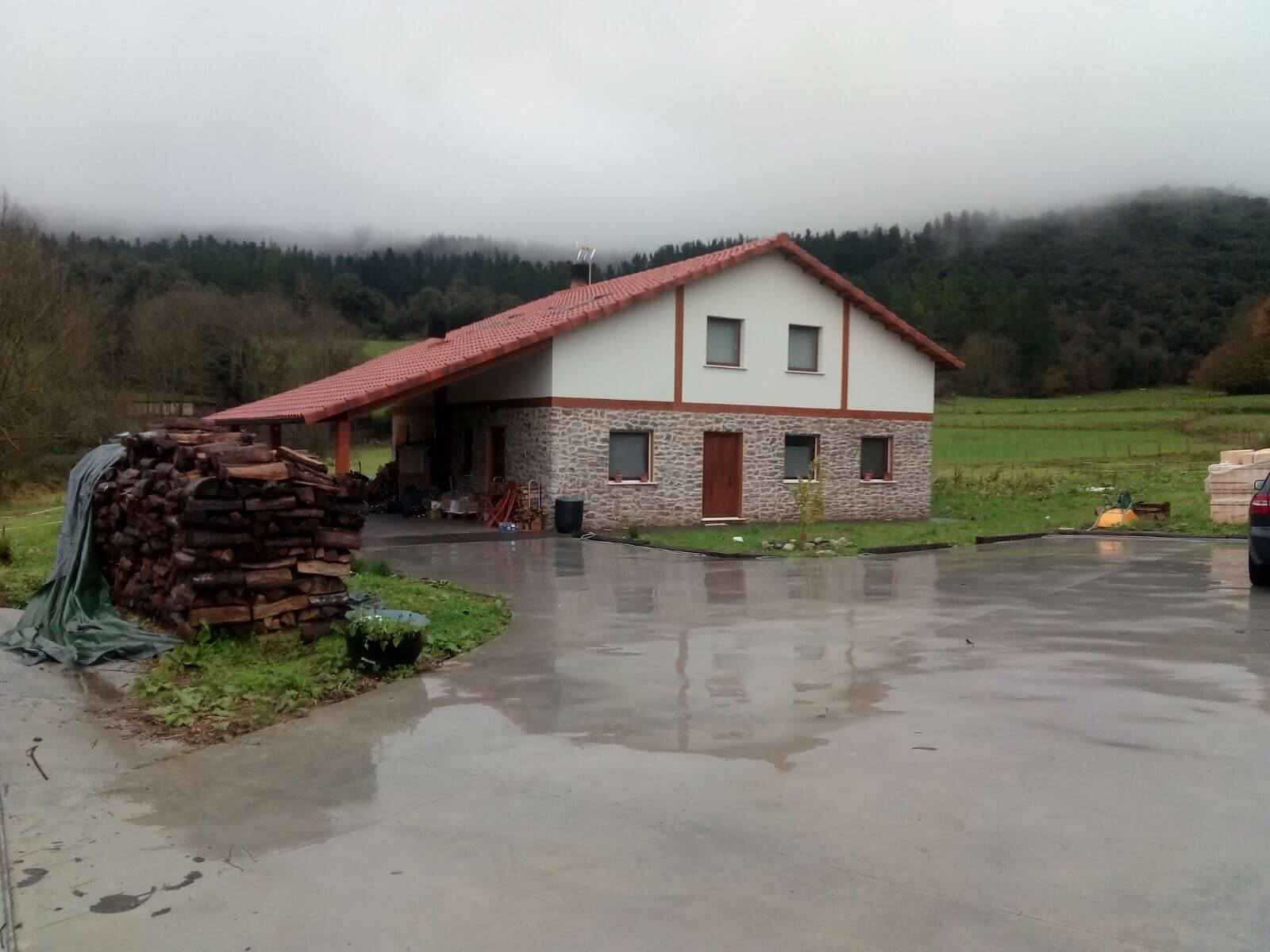 Una casa con techo rojo y una pila de troncos delante de ella.