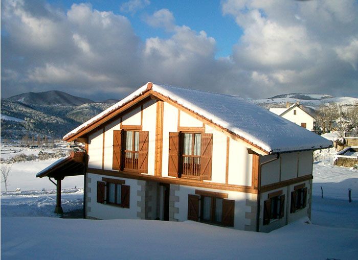 Una casa con nieve en el techo y montañas al fondo.
