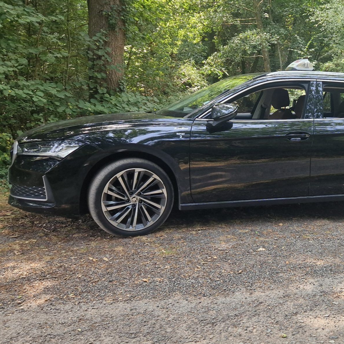 Voiture noire garée sur un chemin de gravier, forêt en arrière-plan.