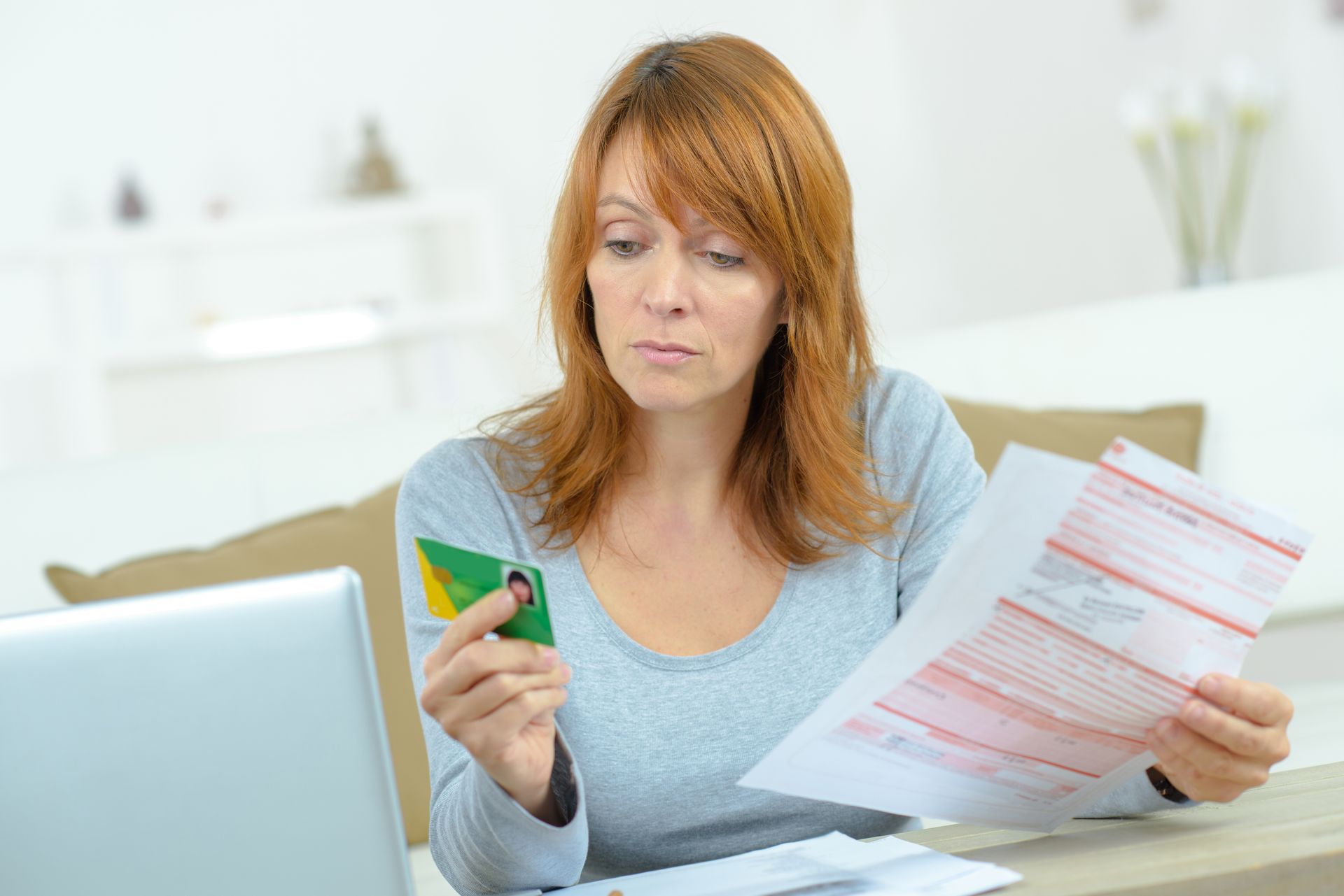 Une femme examine ses factures et sa carte Vitale, l'air soucieux, dans un cadre domestique.