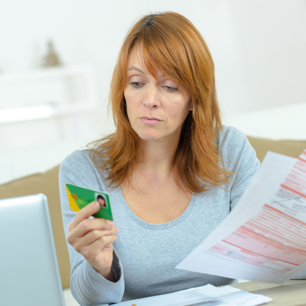 Femme consultant des documents et une carte Vitale. À l'intérieur, expression sérieuse.
