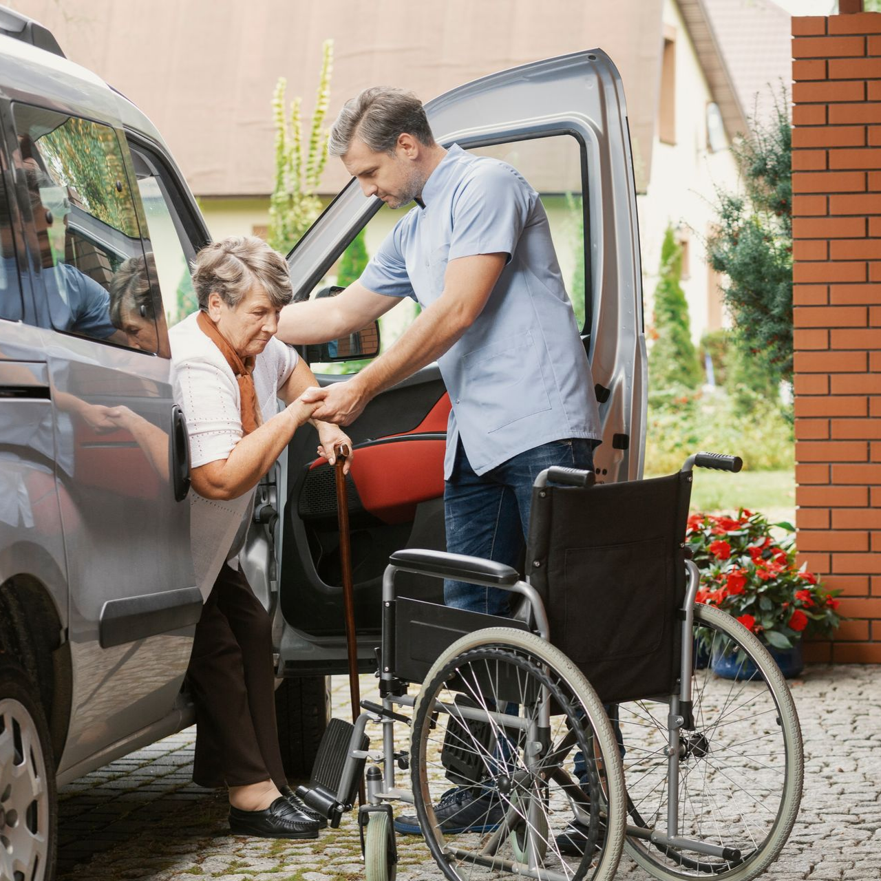 Un homme aide une personne à mobilité réduite à sortir d'une camionnette ; un fauteuil roulant se trouve à proximité.