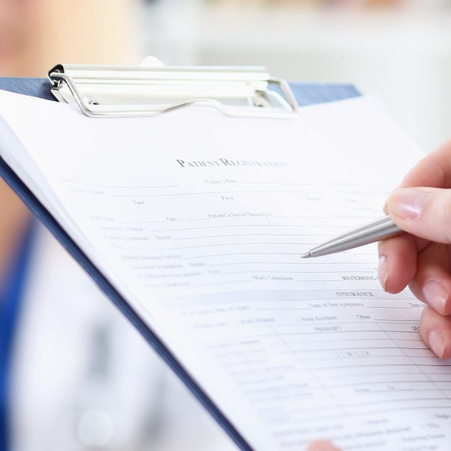 Une personne tenant un bloc-notes avec un formulaire Dossier patient partiellement rempli, prête à écrire au stylo.