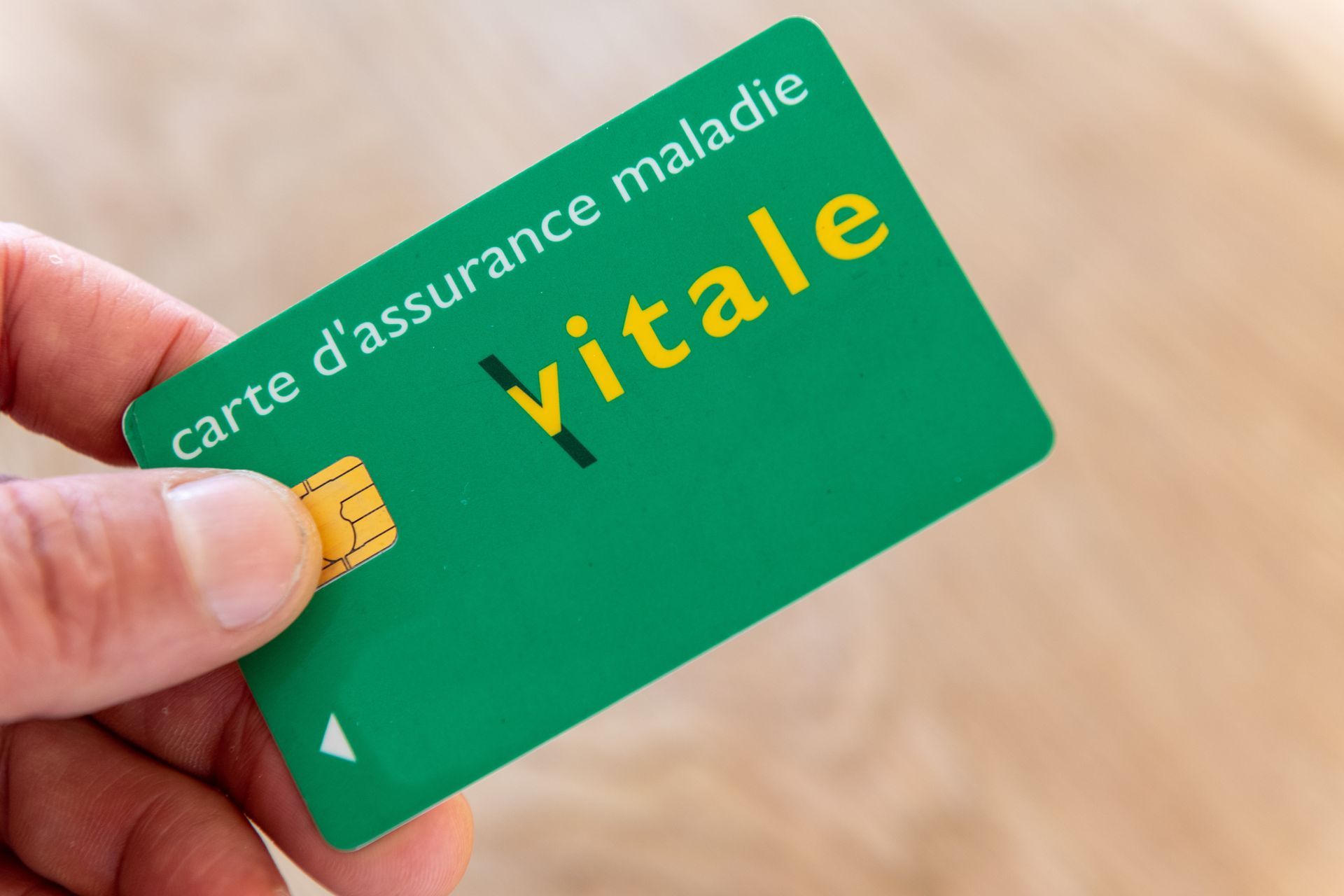 Main tenant une carte Vitale verte, carte d'assurance maladie française.