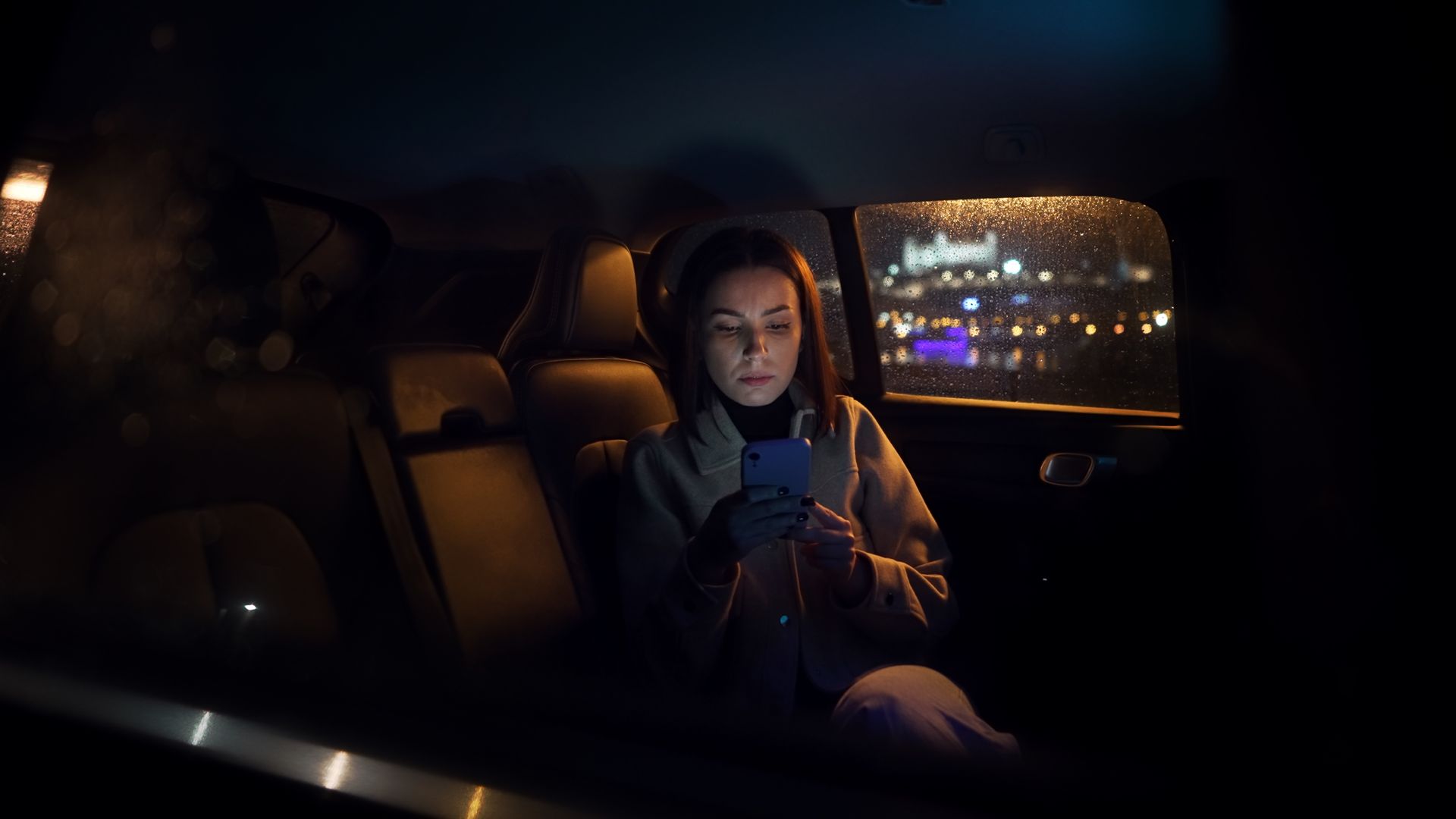 Une femme dans un taxi la nuit, utilise son téléphone.