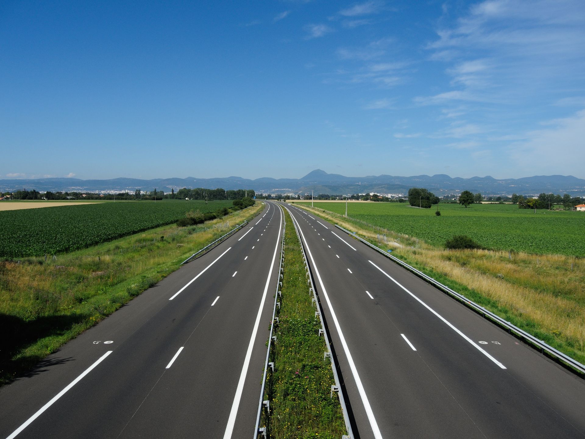 Une route droite à deux voies traverse des champs sous un ciel bleu limpide.