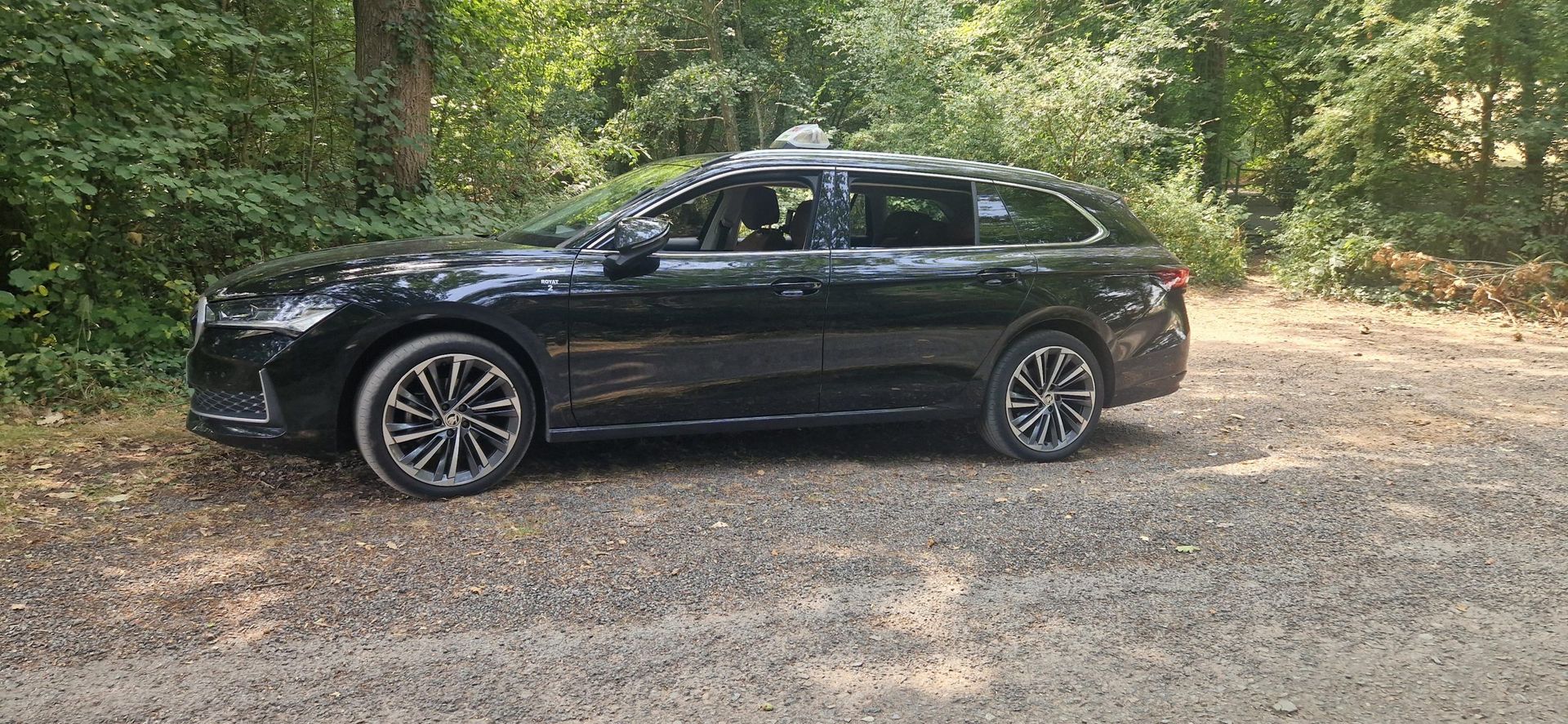 Break noir garé sur un chemin de gravier, arbres en arrière-plan.