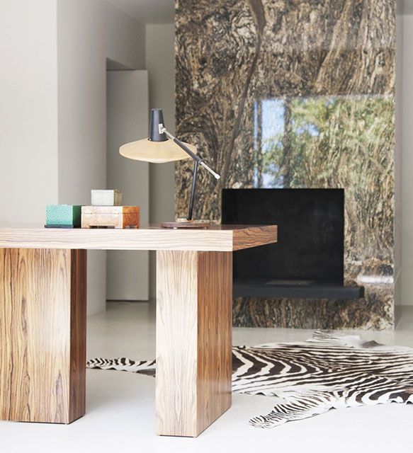 Bureau en bois avec lampe, boîtes et tapis zébré devant une cheminée en marbre.