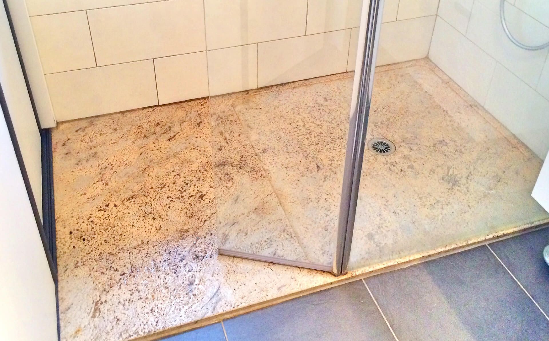 Sol de douche sale, taché de brun et moisi. On aperçoit une porte de douche en verre et des carreaux blancs.