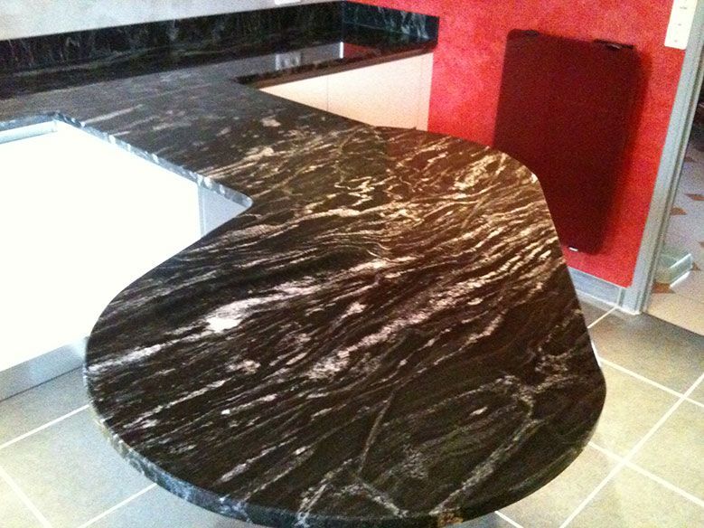 Plan de travail en granit noir veiné de blanc. Cuisine aménagée avec mur rouge et placards blancs.