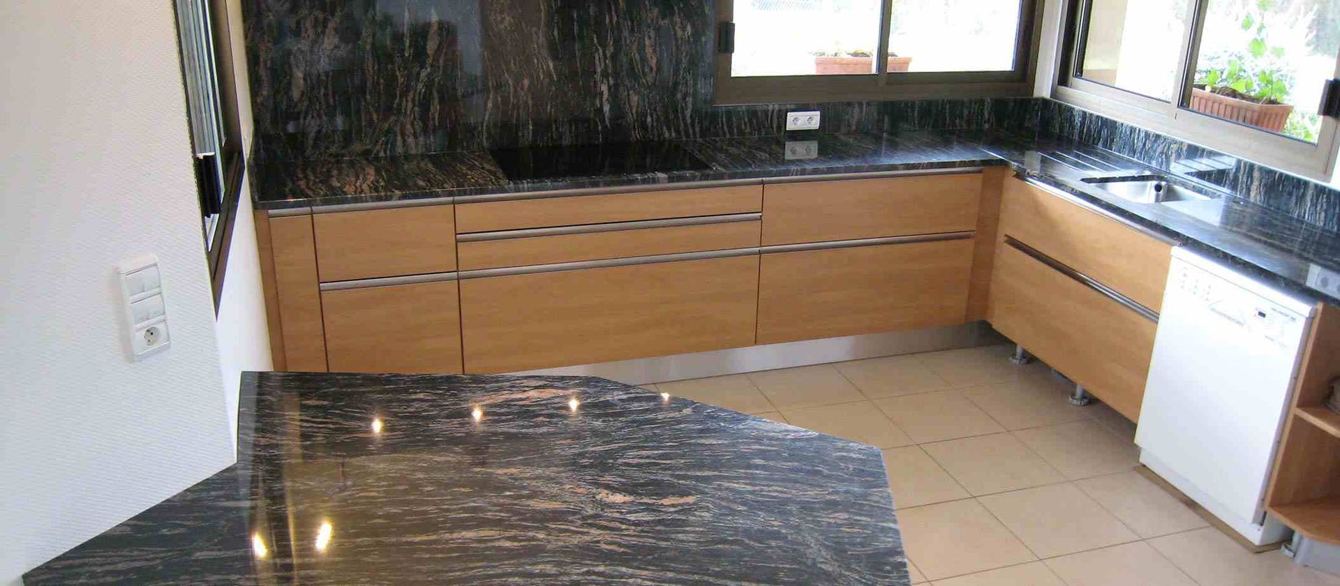 Cuisine moderne avec placards en bois clair, comptoirs en granit noir et sol carrelé.