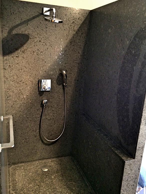 Douche avec murs en pierre sombre, pommeau de douche et douchette.