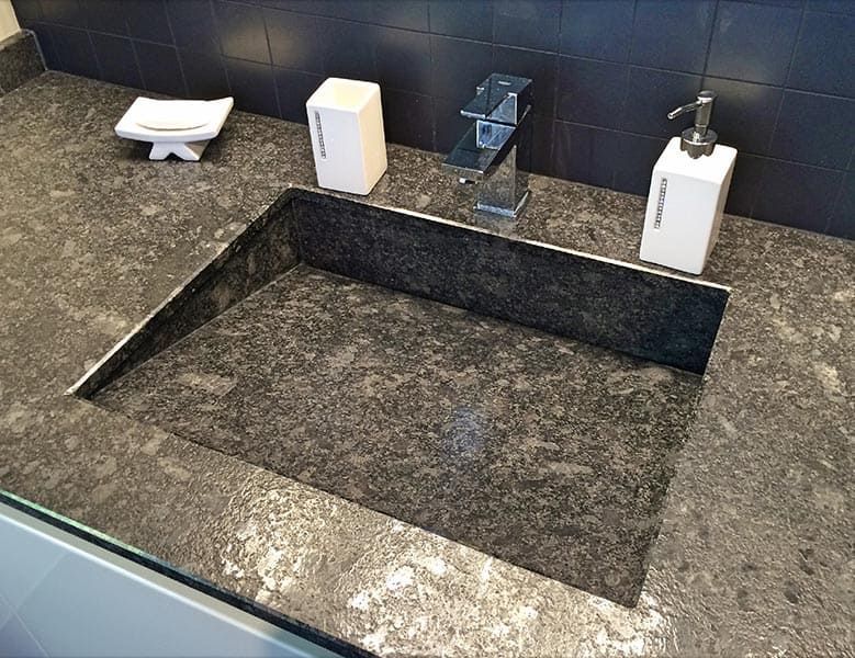 Plan de travail en granit avec évier rectangulaire intégré, distributeurs de savon noir et blanc, robinet chromé.