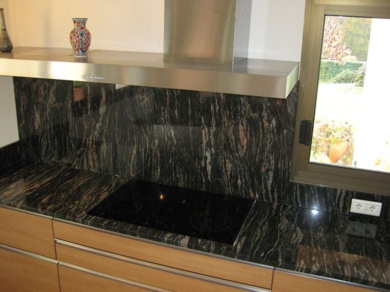 Cuisine avec comptoirs en granit noir, plaque de cuisson et hotte en acier inoxydable.