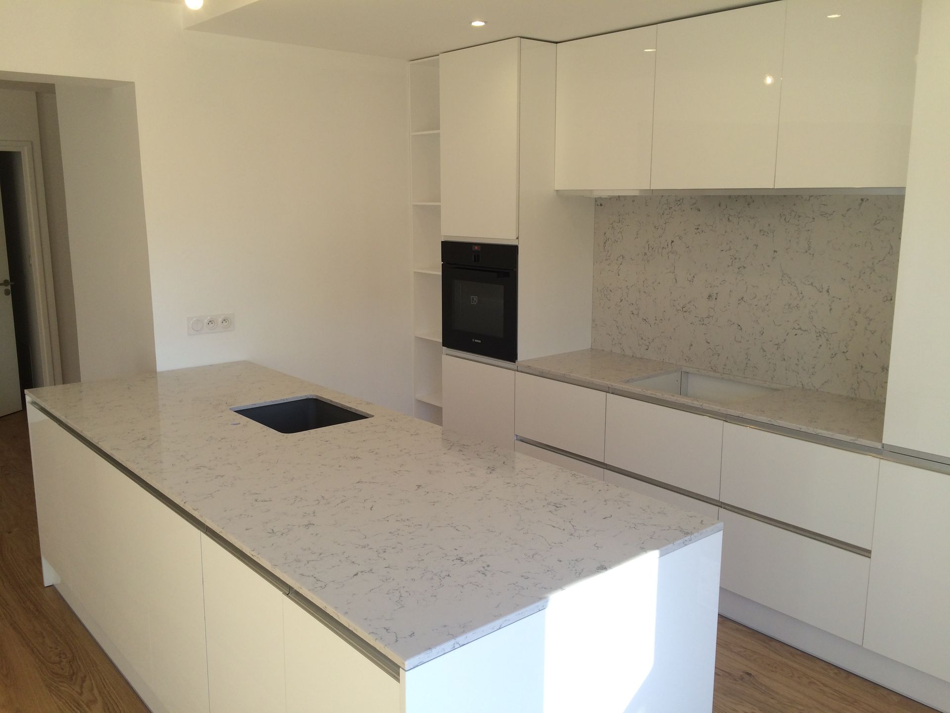 Cuisine moderne blanche avec îlot central, four encastré et comptoirs clairs mouchetés.