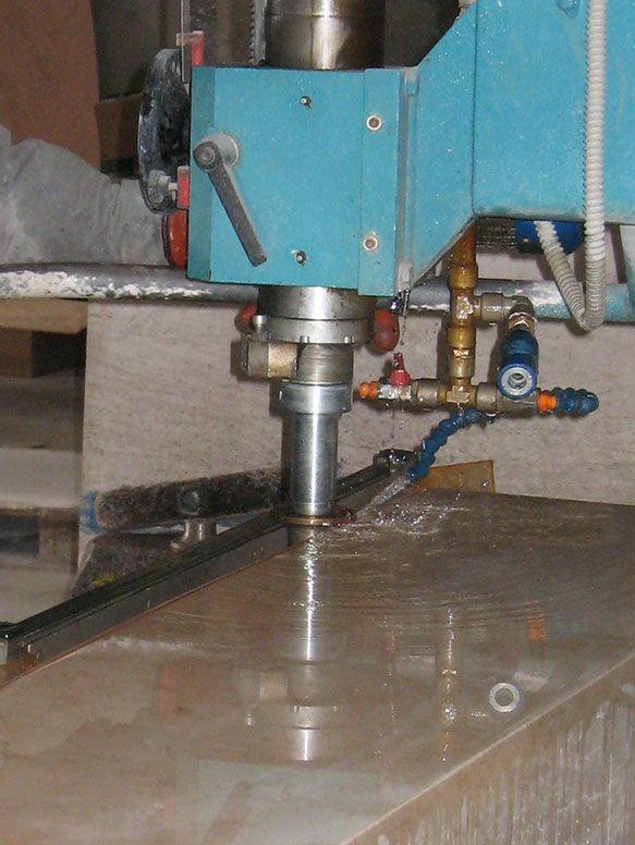 Une machine bleue découpe une dalle de pierre en pulvérisant de l'eau.