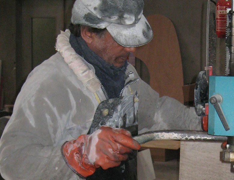 Personne utilisant une machine, couverte de poussière blanche, portant des gants et un chapeau.