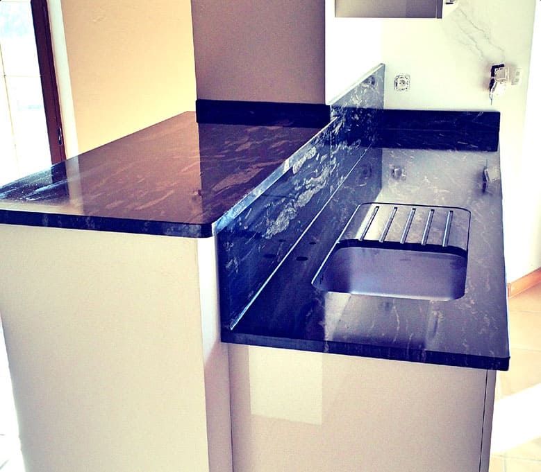 Plan de travail de cuisine en granit foncé, placards blancs et évier intégré.