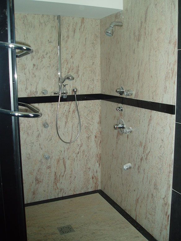 Cabine de douche avec murs à motif marbre, plusieurs pommes de douche, robinetterie chromée et finitions foncées.