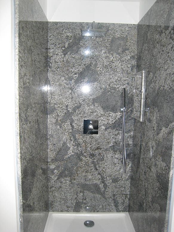 Cabine de douche avec carrelage mural gris imitation granit, robinetterie chromée et receveur de douche blanc.
