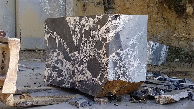 Gros bloc de marbre gris et blanc, fraîchement taillé et présentant des fractures visibles, dans une carrière.