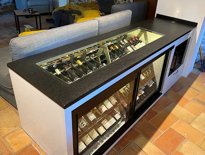 Bar à vin blanc sur mesure avec vitrine réfrigérée intégrée, surmonté d'un comptoir noir et d'un casier à vin en verre encastré.