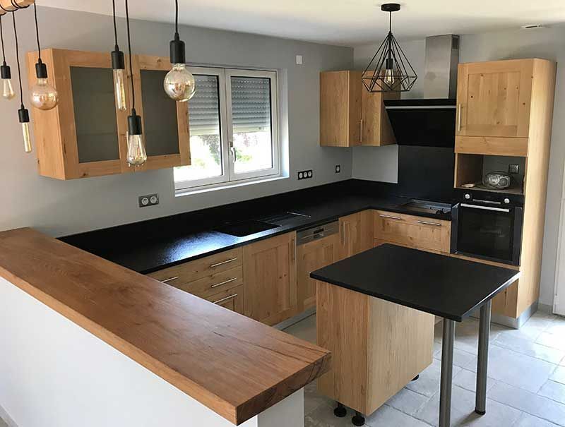 Cuisine moderne avec placards en bois clair, plans de travail noirs et un petit îlot.