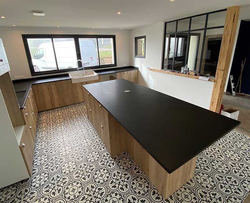Cuisine moderne avec comptoirs noirs, armoires en bois et carrelage à motifs au sol.