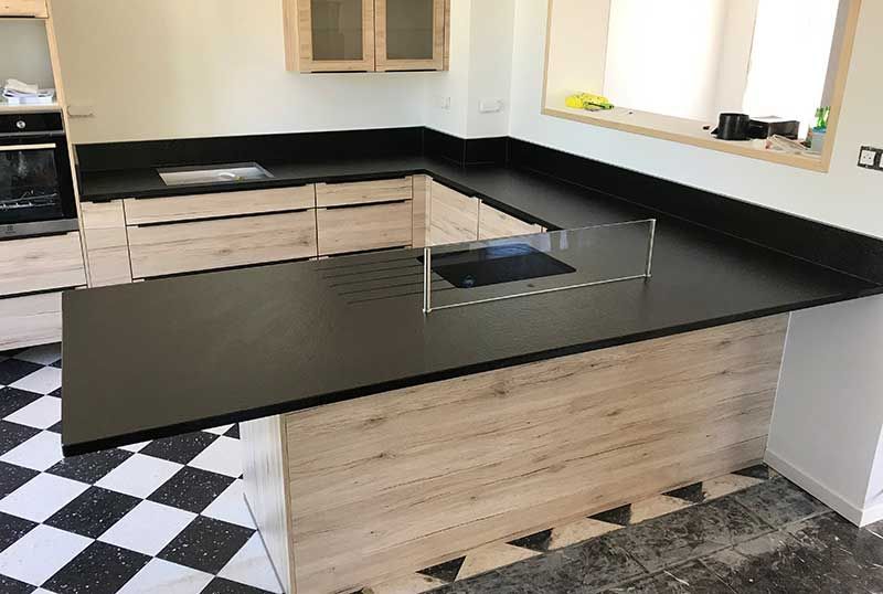 Cuisine moderne avec placards en bois clair, plans de travail noirs et sol à damier.