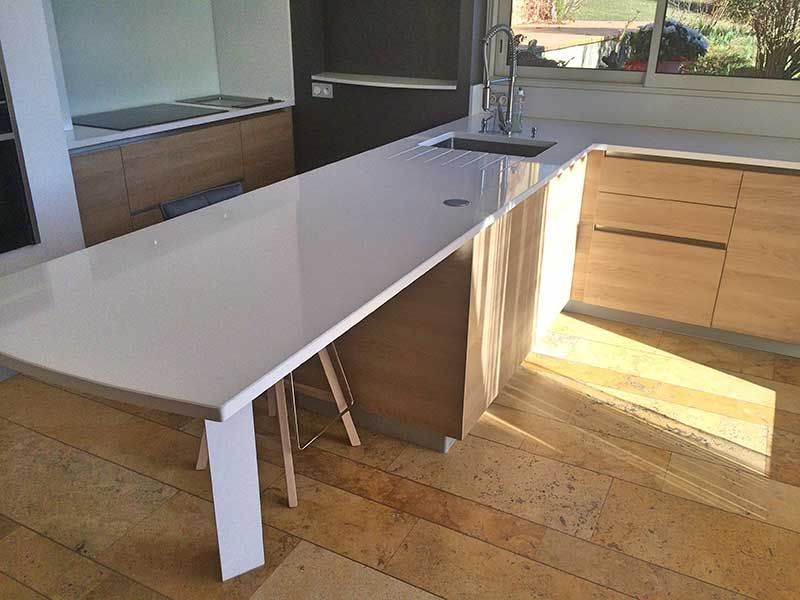 Cuisine moderne avec comptoirs blancs, armoires en bois et évier.