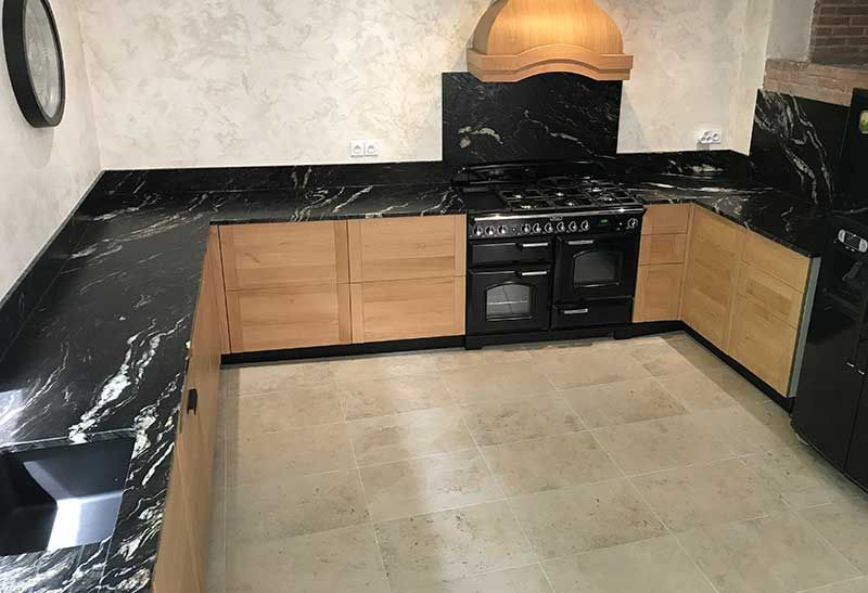 Cuisine en forme de U avec comptoirs en granit noir, armoires en bois et cuisinière noire.