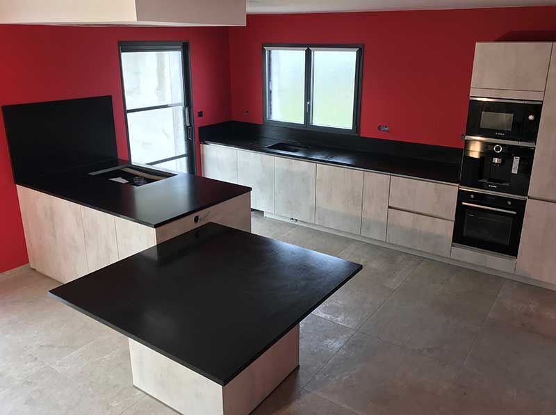 Cuisine moderne avec murs rouges, sols gris, placards en bois clair et plans de travail noirs.