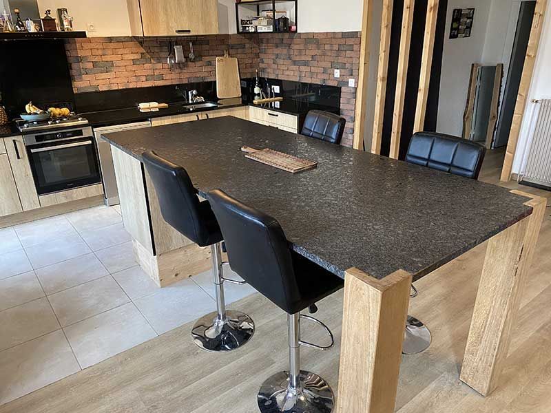 Cuisine avec îlot central au plan de travail foncé, tabourets de bar et éléments en bois.