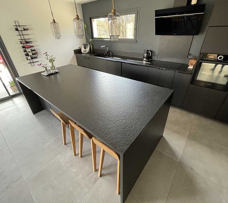 Cuisine moderne noire avec un grand îlot central, des tabourets et des suspensions lumineuses.