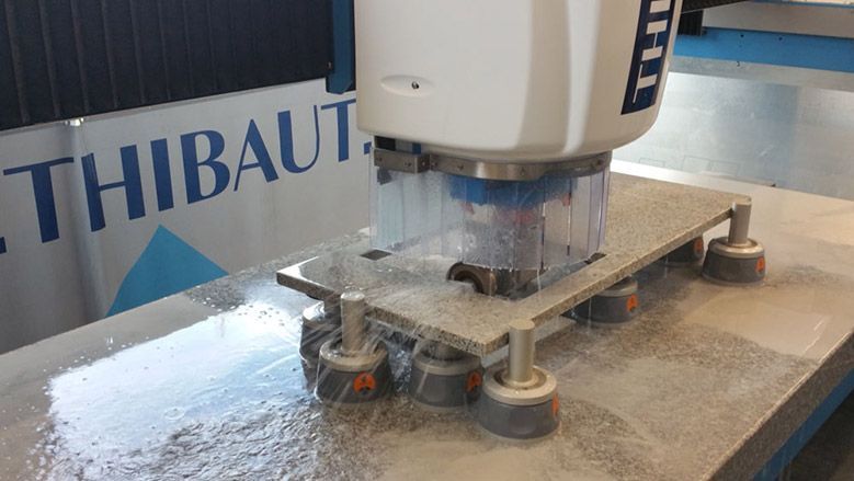 Une machine rectifiant une dalle de pierre par pulvérisation d'eau, à l'intérieur d'une usine.