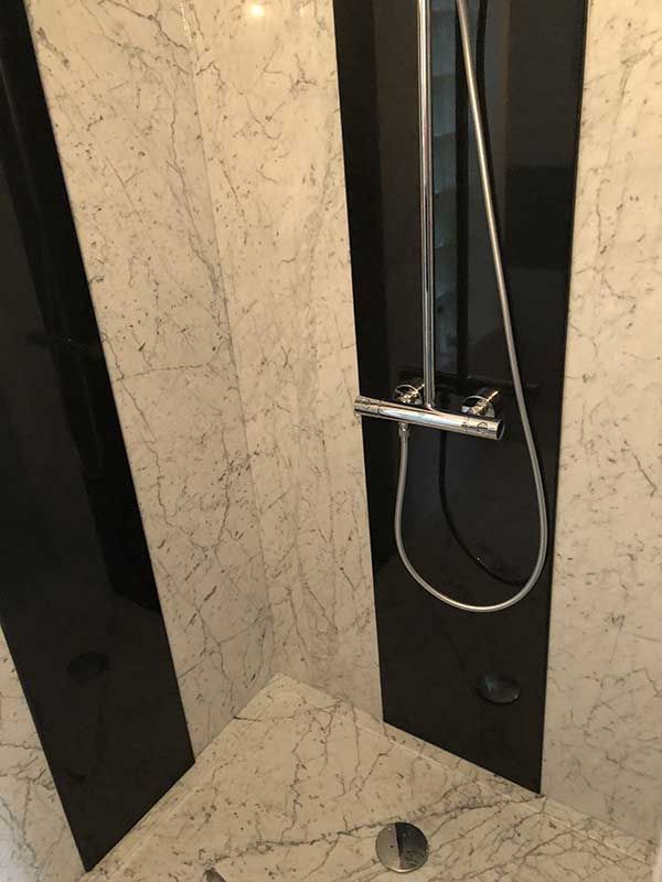 Douche avec parois en marbre noir et blanc et pommeau de douche chromé.