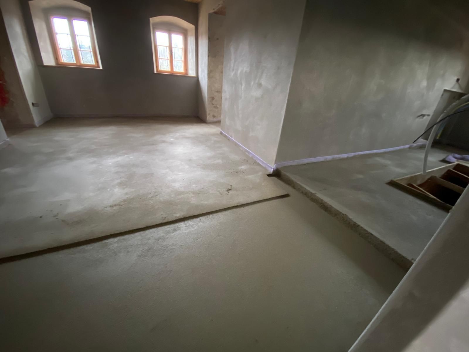 Ein Raum mit Betonboden und vielen Fenstern.